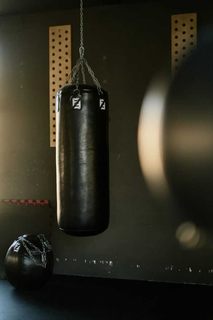 Black punching bag hangs in a gym, bathed in sunlight, creating a moody and focused atmosphere.